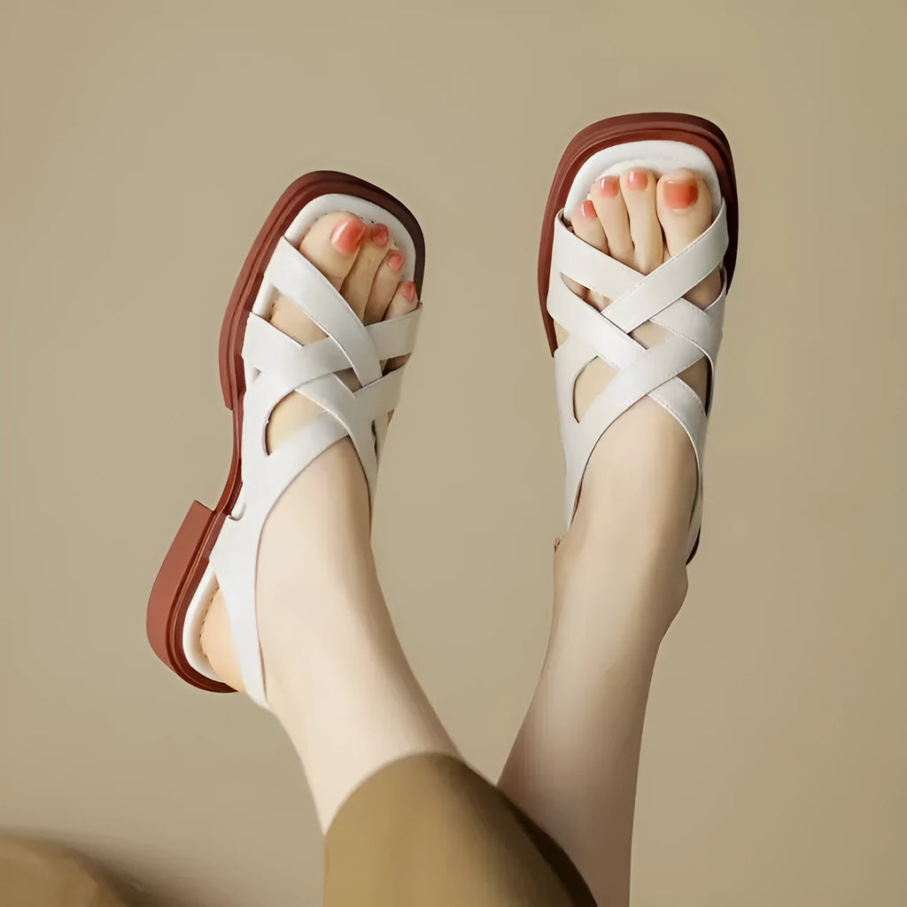 Women's glossy patent leather sandals with a square toe and low heel on a solid colour background.