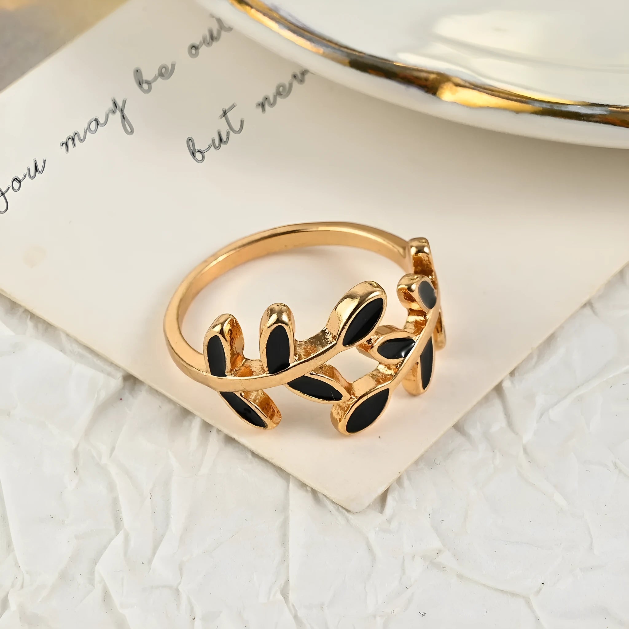 Gold electroplated acrylic ring with a geometric leaf and flower design on a model's index finger.