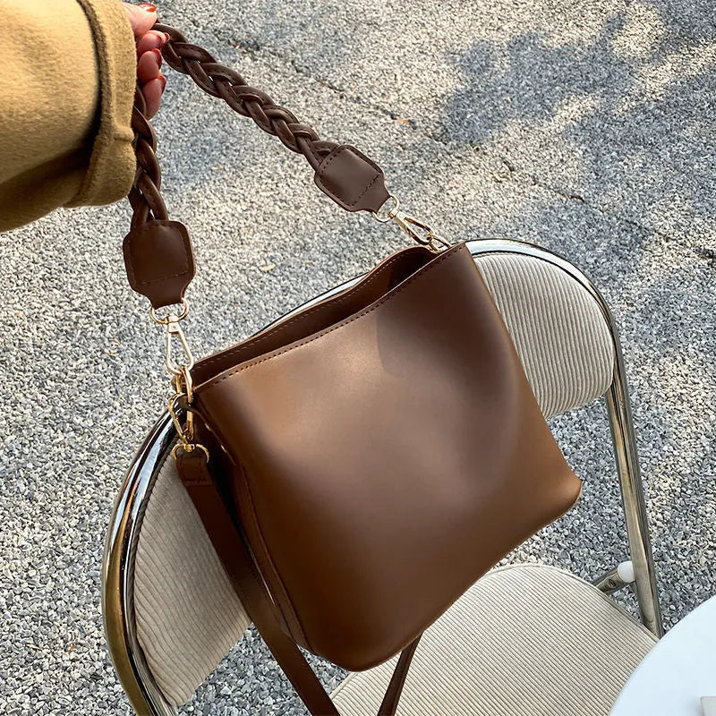 Khaki woven crossbody bucket bag with a buckle, shown on a model for scale