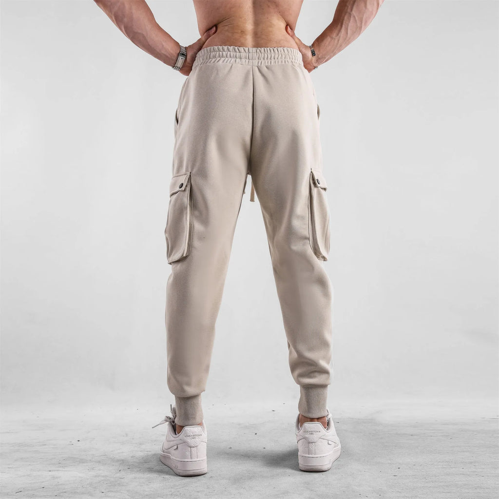 Men's loose-fit beige cotton trousers with tied ankle cuffs and multiple pockets on the legs.