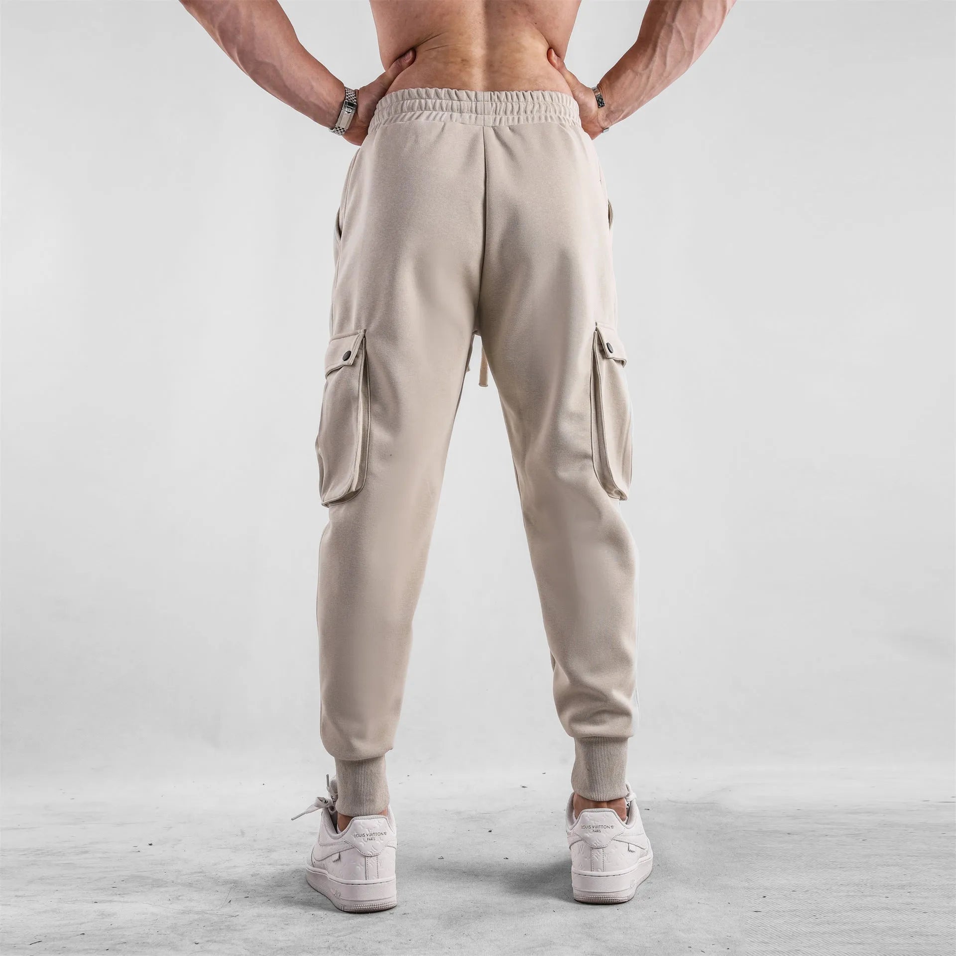 Men's loose-fit beige cotton trousers with tied ankle cuffs and multiple pockets on the legs.