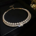 A silver geometric collar necklace resting on a surface, showing its curved clavicle chain design.