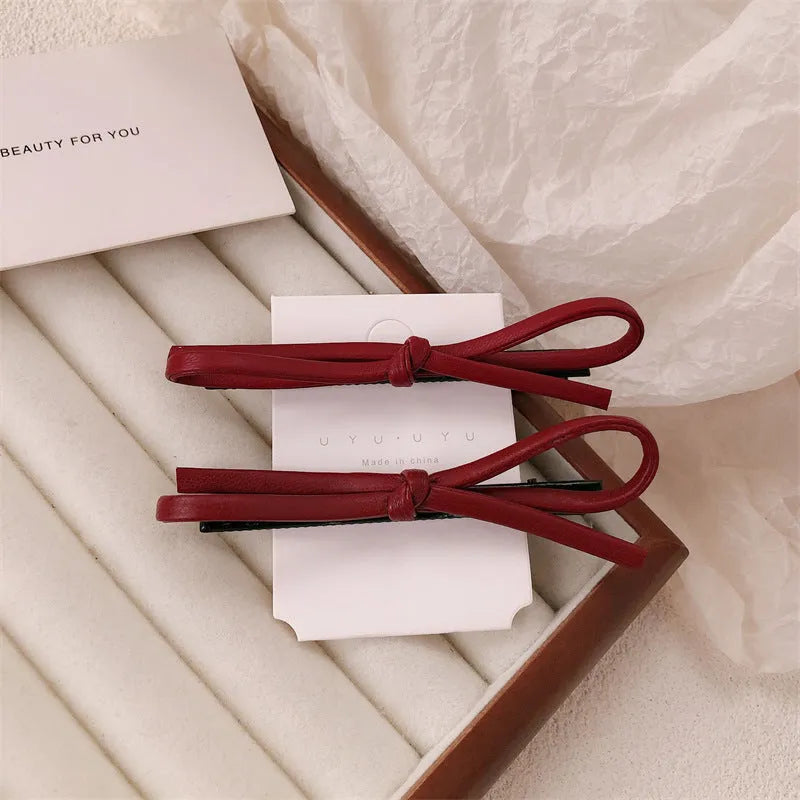 Wine red genuine leather bow attached to a metal hair clip, shown on a background.