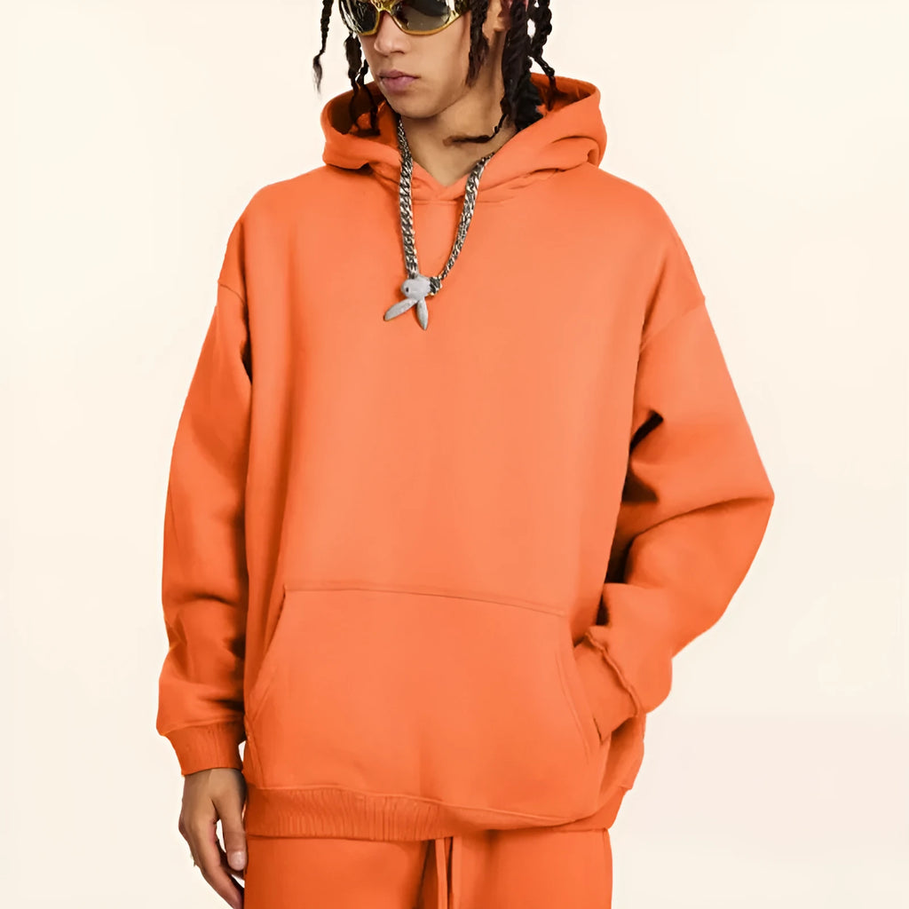 A man wearing a loose-fit, grey cotton terry hooded sweater with drop-shoulder sleeves.
