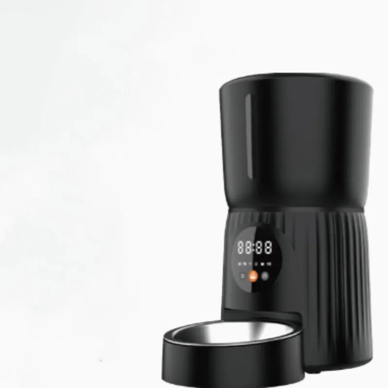 Black automatic pet feeder with digital display and food bowl on a kitchen counter.