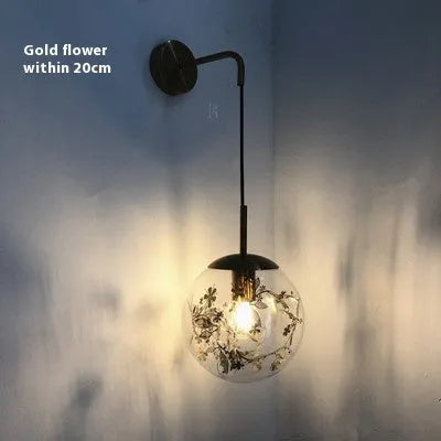 Modern simple glass bedside wall lamp in silver or gold finish on a white wall.