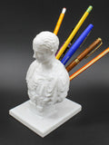 White resin sculpted character pen holder on a desk, holding pens and pencils.