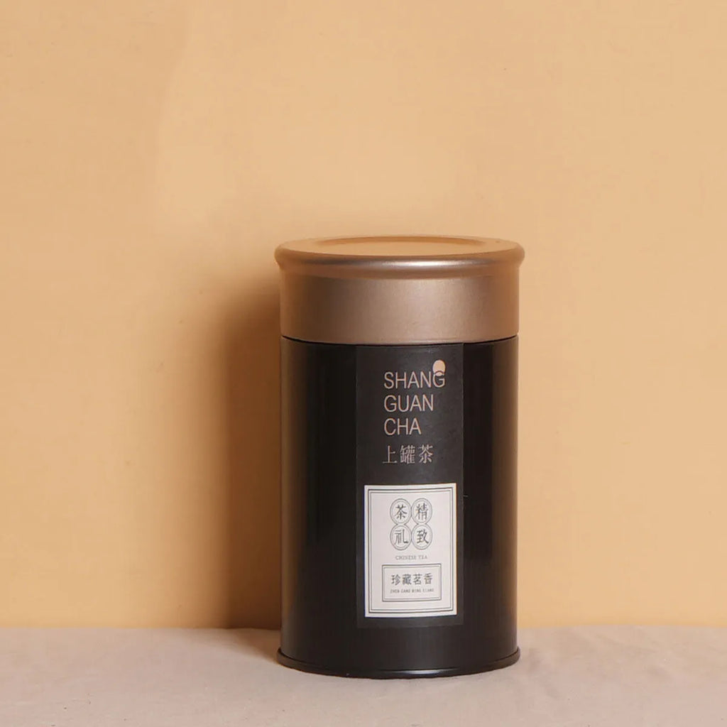 Green tinplate sealed tea storage box with black lid on a wooden surface.