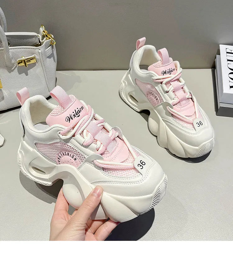 Women's pink sneakers with a cross strap and thick sole on a neutral background.
