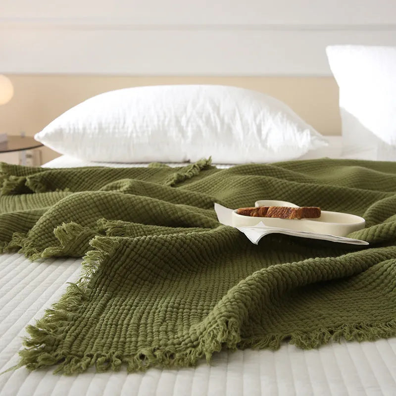 Four-layer gauze cotton blanket with tassel edging in avocado green, laid flat.
