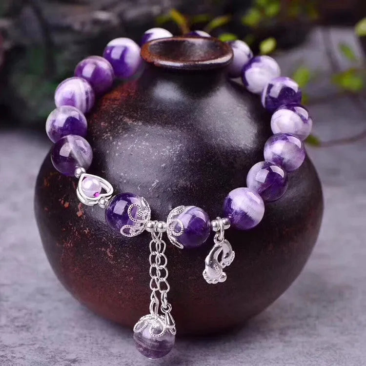 Women's amethyst bracelet with 10mm round purple beads on a wrist.