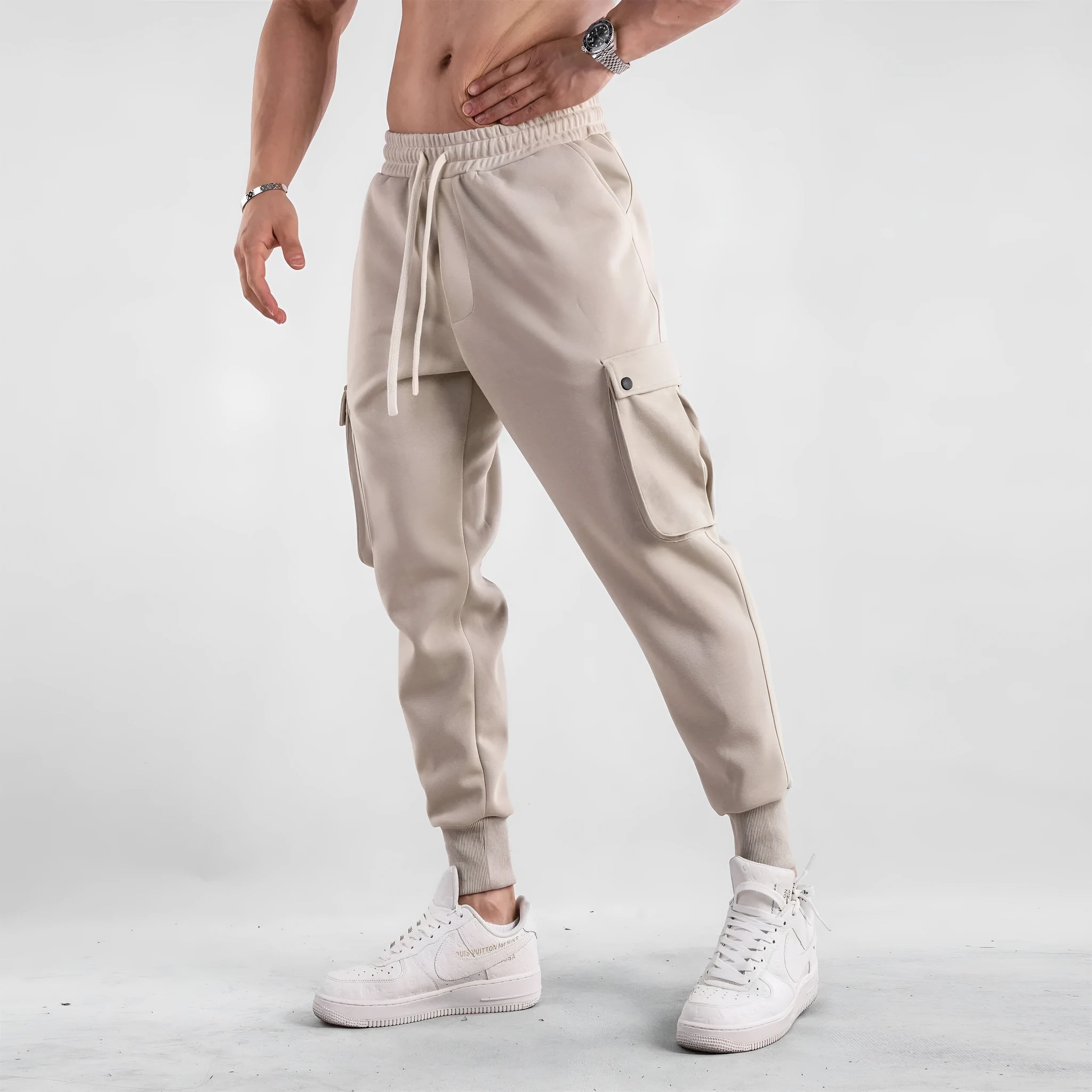 Men's loose-fit beige cotton trousers with tied ankle cuffs and multiple pockets on the legs.