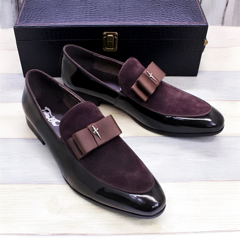 Men's black tassel loafers with glossy patent leather upper and matte leather toe holder on a wooden floor.