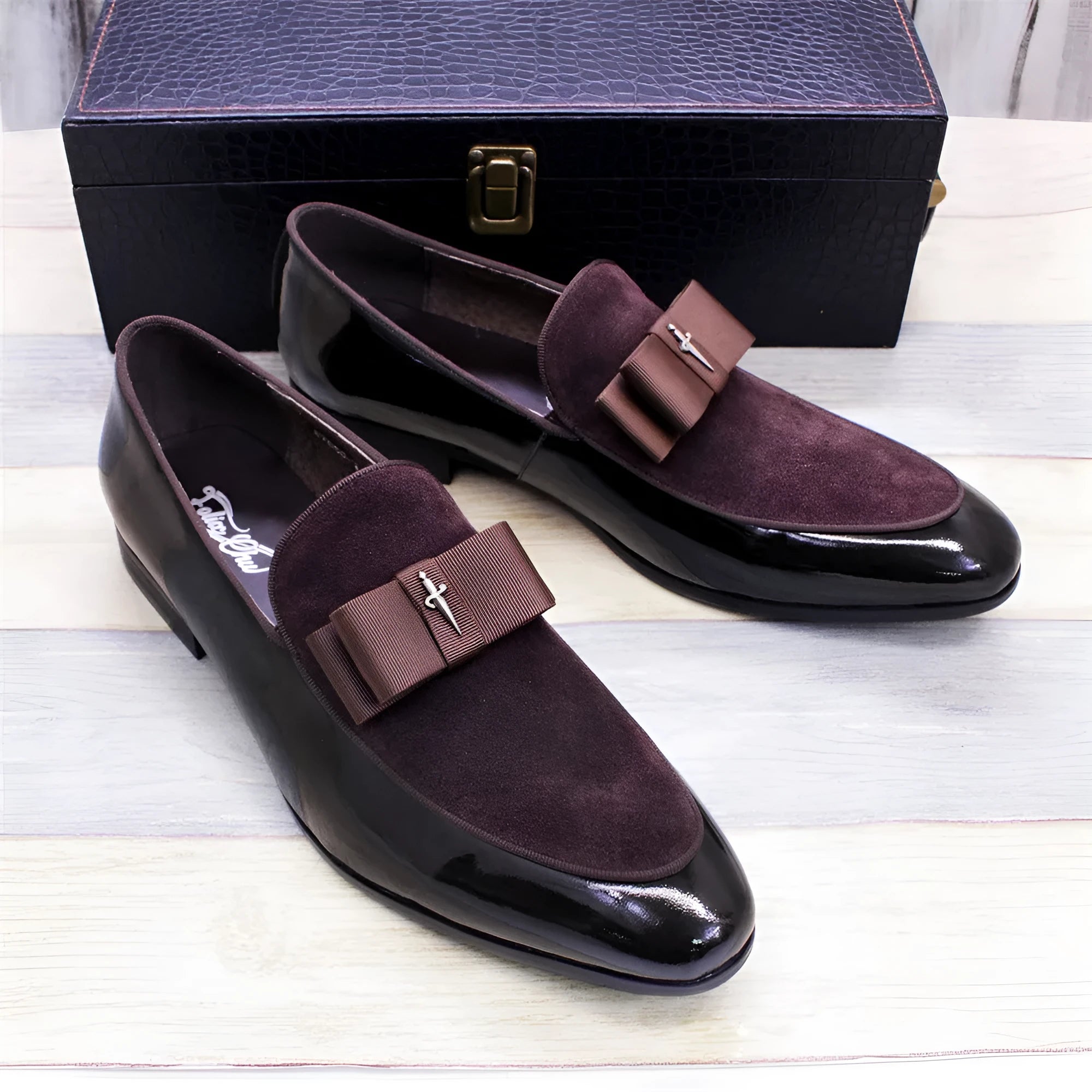 Men's black tassel loafers with glossy patent leather upper and matte leather toe holder on a wooden floor.