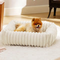 Beige plush pet bed with raised bolster sides for cats and dogs, shown in a home setting.