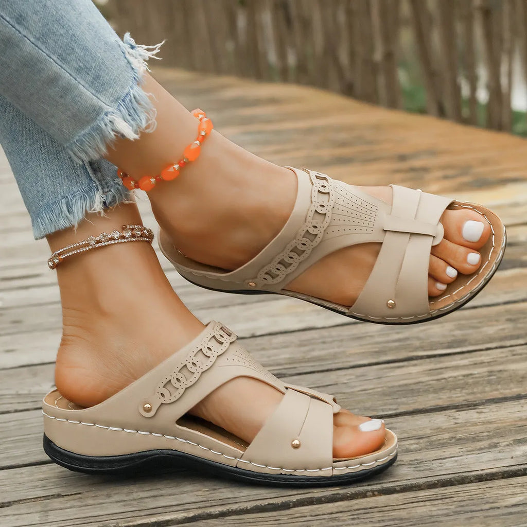 Pair of beige Roman style slippers with a fish mouth toe holder and slope heel on a rubber sole.