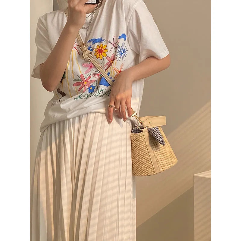 Women's medium beige PU bucket straw bag with open top and messenger strap on neutral background