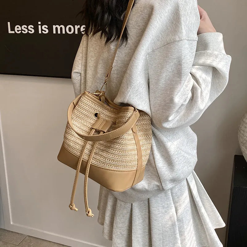 Brown woven straw women's crossbody bucket bag with adjustable strap on a table.