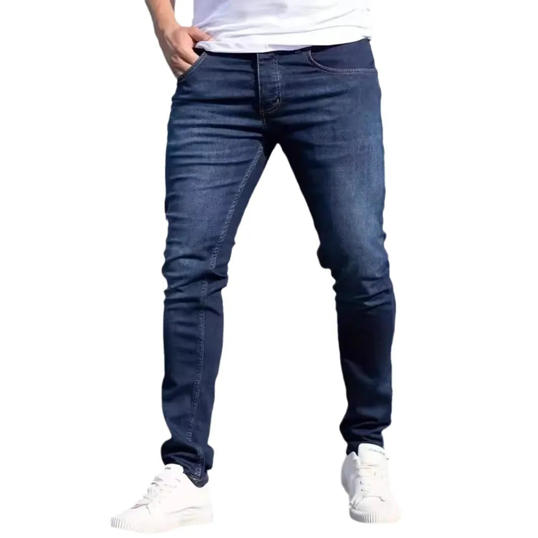 Man wearing dark blue slim fit skinny jeans with a mid-rise waist and zipper fly.