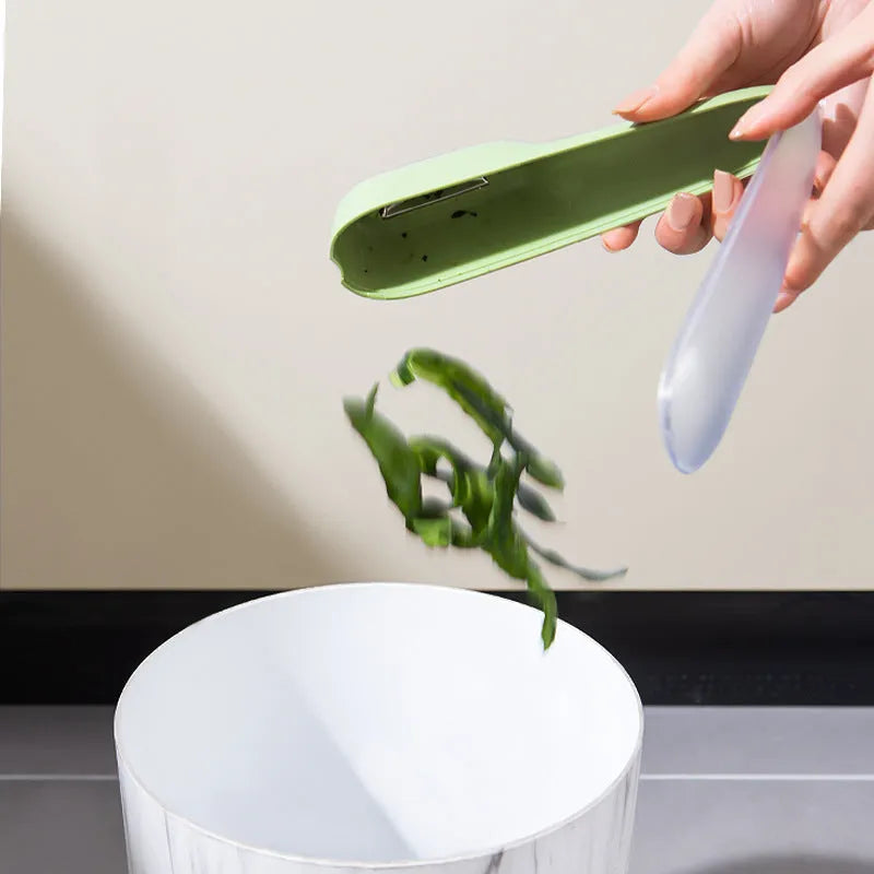 Dark green kitchen peeler with a storage tube extended, showing the stainless steel blade and a hanging hole on the handle.