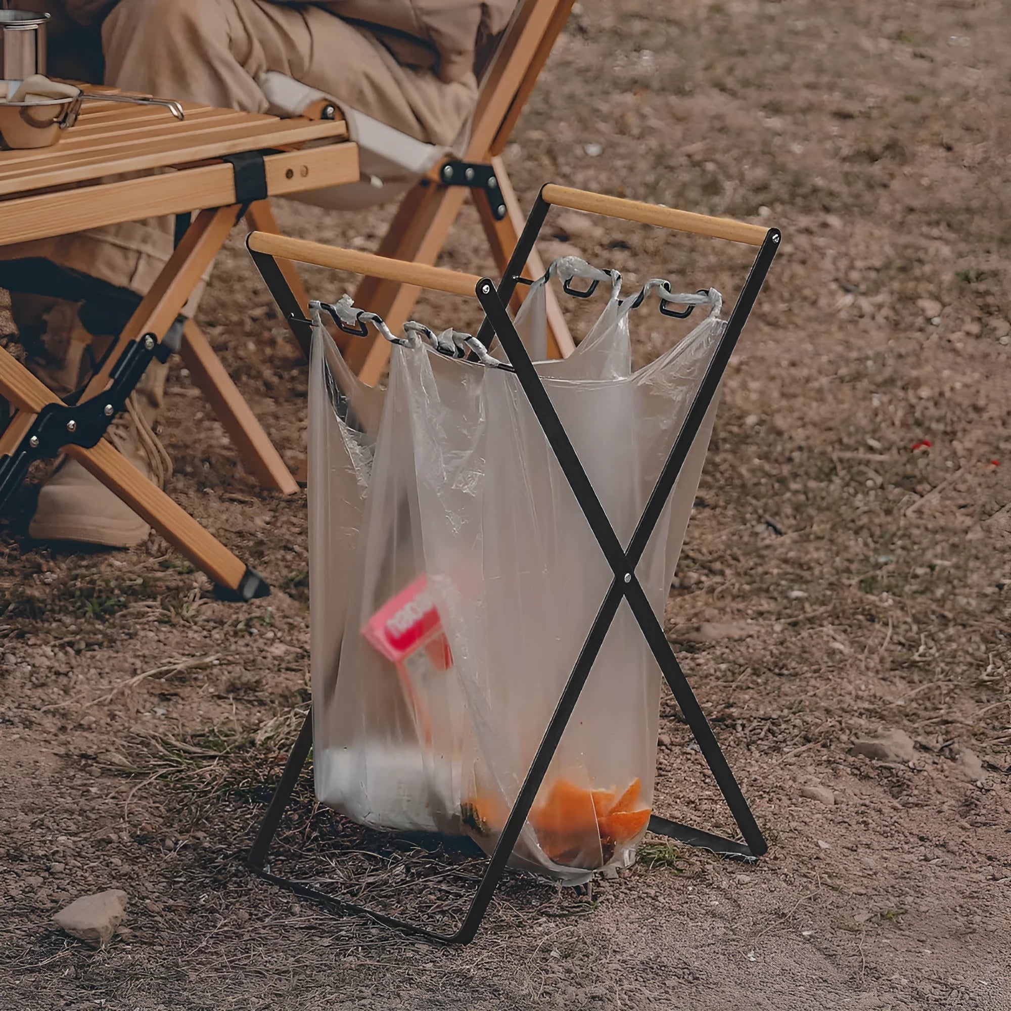 Outdoor black iron folding garbage storage hanger with wooden handle holding a bin bag.