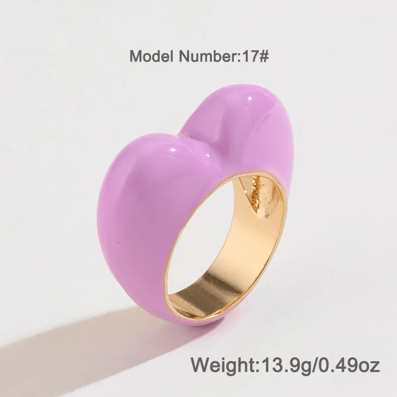 Heart-shaped zinc alloy ring with three-dimensional enamel colour in black, pink, purple, or red on a finger.
