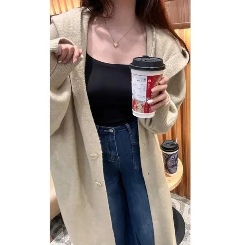 A woman wearing a long, loose, hooded knitted cardigan in a solid colour, demonstrating its below-the-knee length.