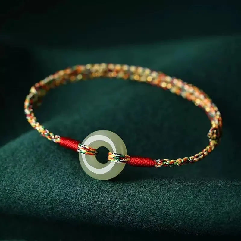 Close-up of a colourful woven rope bracelet with a silver peace buckle clasp on a wrist.