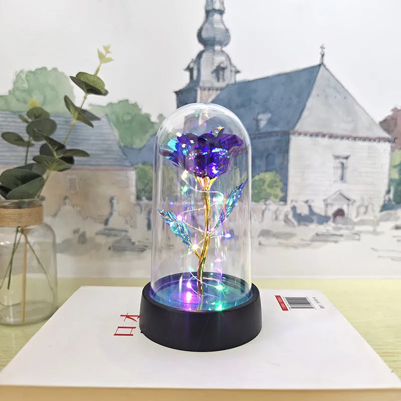 Small glass dome night lamp with plastic flowers on a black base, showing coloured light illumination.