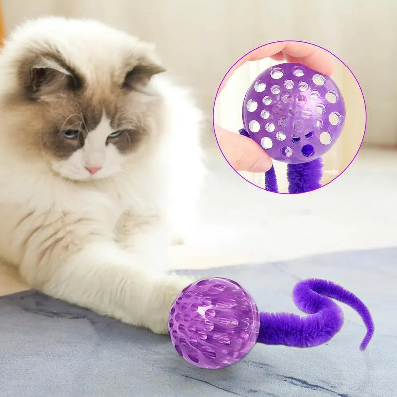 Green bouncy worm-shaped cat toy with a long plush tail on a wooden floor.