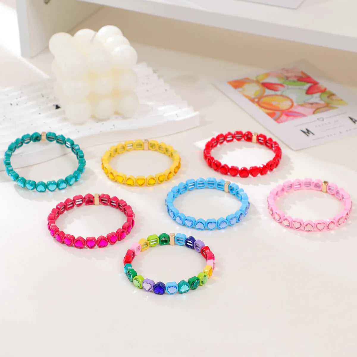 Colourful enamel heart-shaped stretch bracelet on a wrist showing the alloy and elastic band construction.