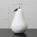 A black resin apple figurine and a white resin pear figurine on a wooden surface.