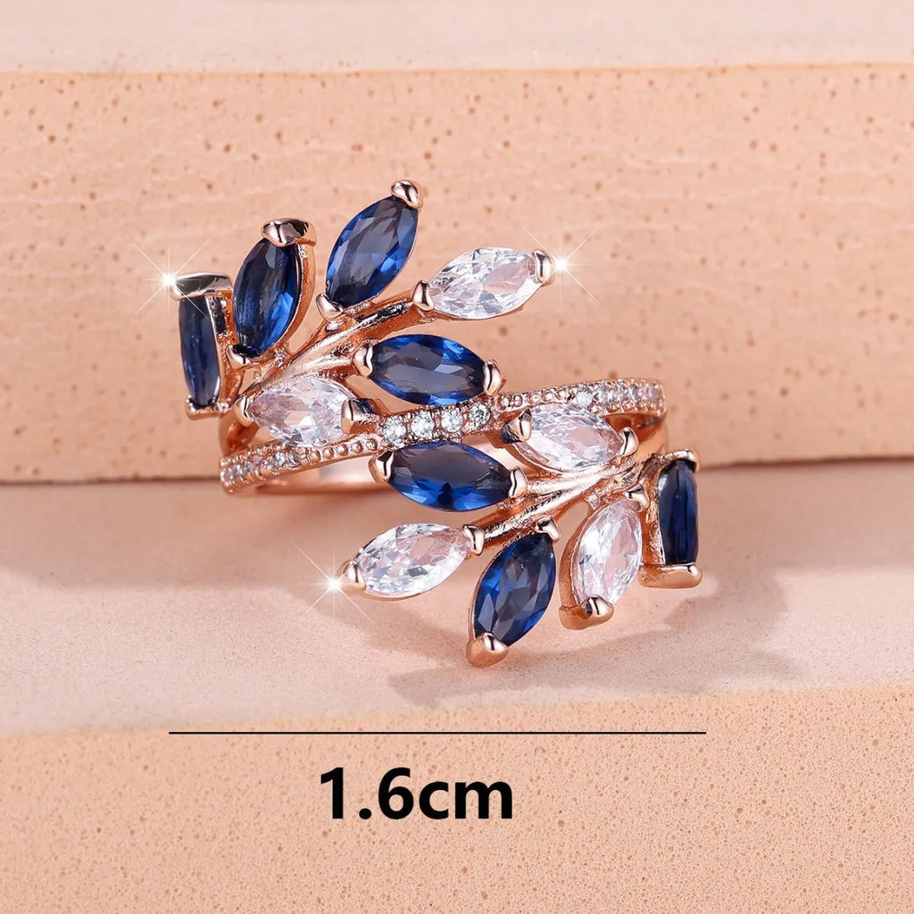 Adjustable open-ended copper ring with leaf design and central blue zircon stone on a finger.