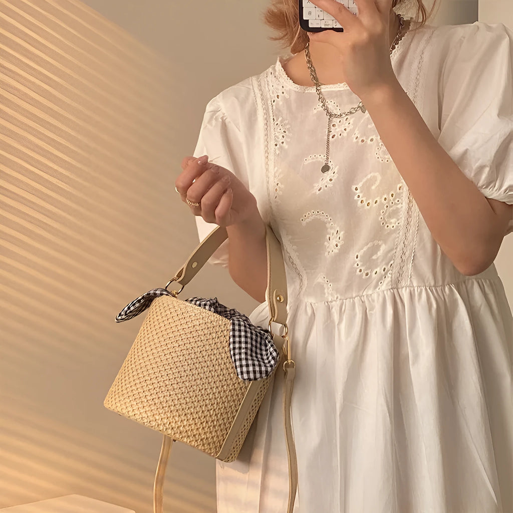 Women's medium beige PU bucket straw bag with open top and messenger strap on neutral background