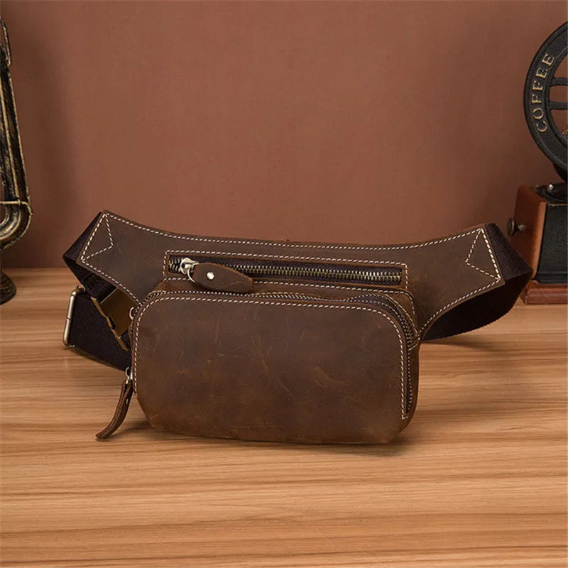 Brown top-layer cowhide men's sports waist bag shown with a 10-inch laptop and phone next to it for scale.