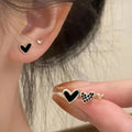 Three pairs of heart-shaped alloy earrings in gold, black, black and white, and pink colours