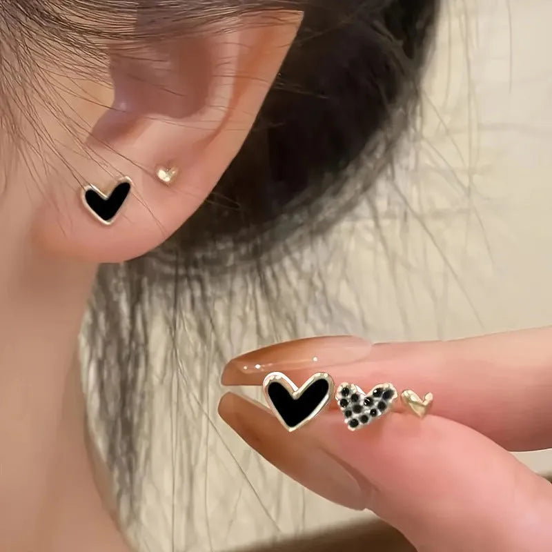 Three pairs of heart-shaped alloy earrings in gold, black, black and white, and pink colours