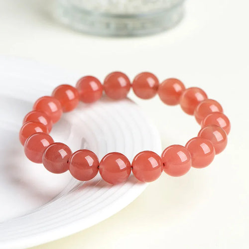 A close-up of a polished cherry red agate bead bracelet on a wrist.
