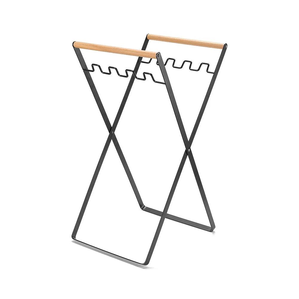 Outdoor black iron folding garbage storage hanger with wooden handle holding a bin bag.