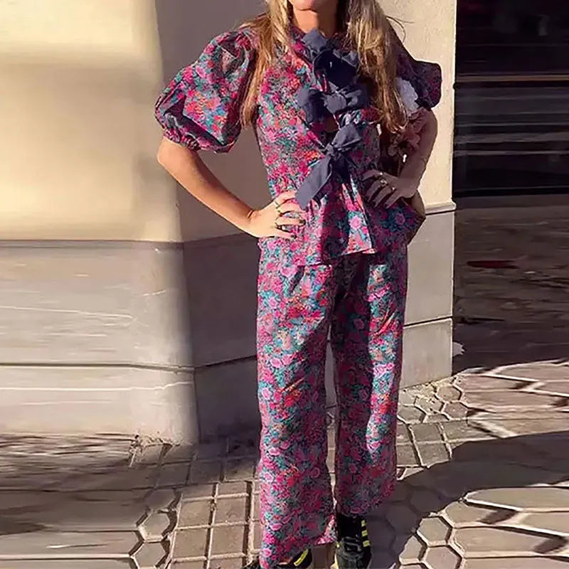Women's floral printed trousers suit with a tie-neck blouse featuring puff sleeves and matching trousers.