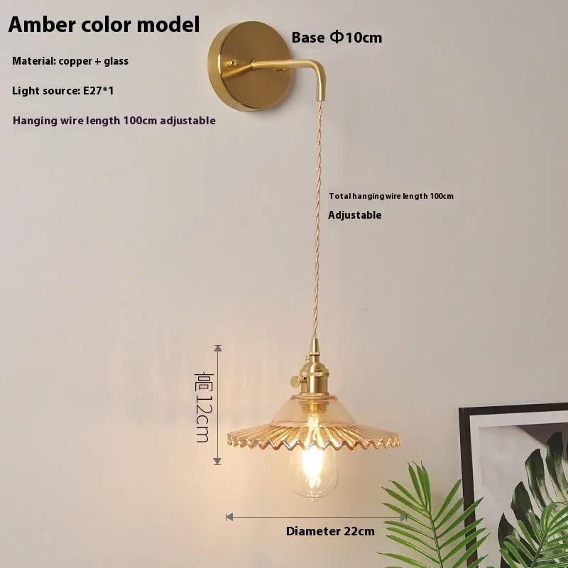 Brass wall lamp with an adjustable smoked grey glass lotus shade mounted beside a bed.