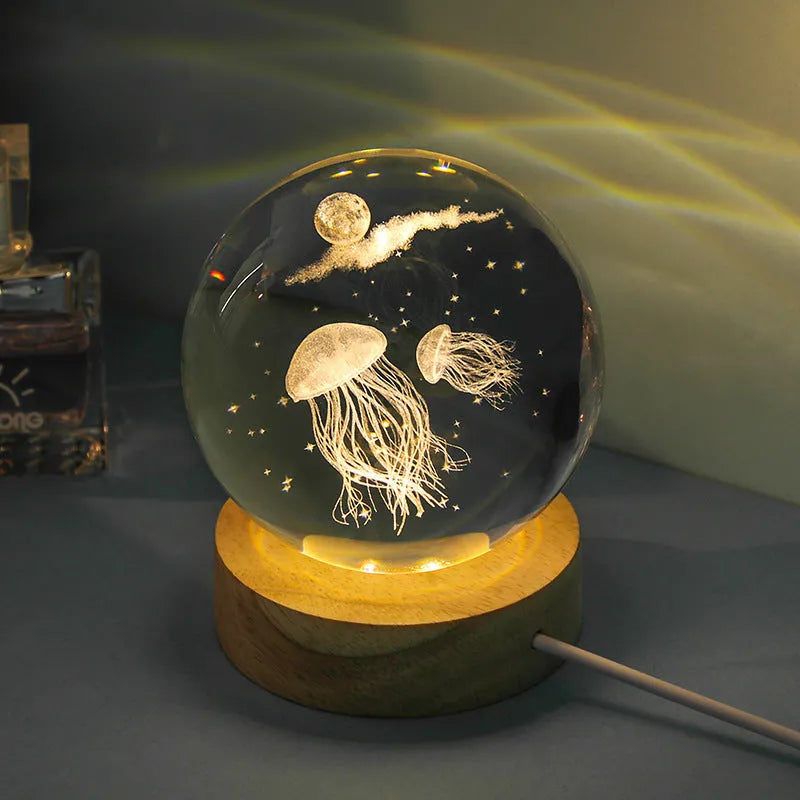 Transparent crystal ball night lamp with 3D carved jellyfish design, lit with soft blue glow on a round base.