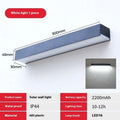 Black solar-powered outdoor wall lamp with integrated solar panel, mounted on a garden wall.