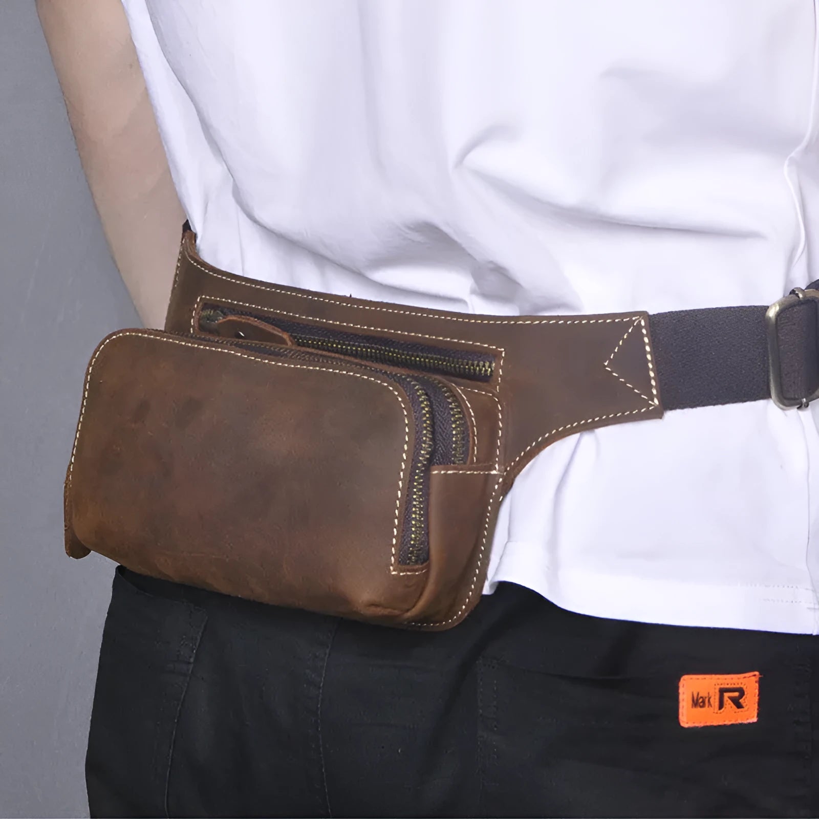 Brown top-layer cowhide men's sports waist bag shown with a 10-inch laptop and phone next to it for scale.