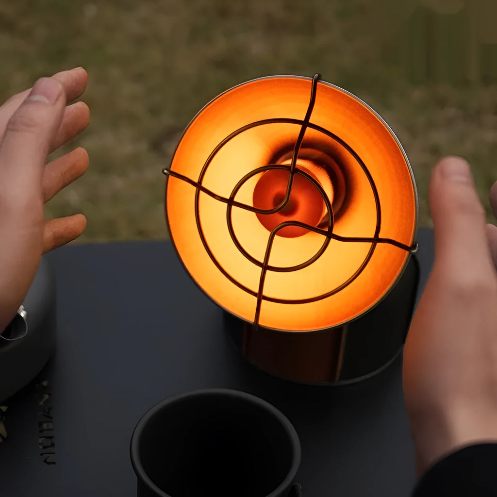 Black and orange portable camping stove with automatic ignition on a rocky outdoor surface.
