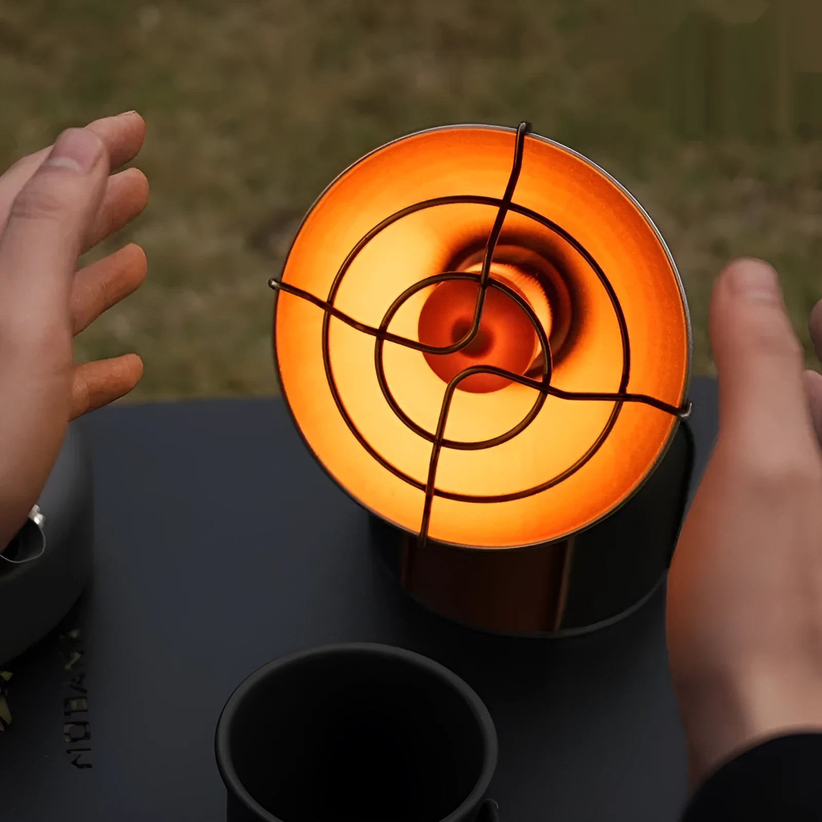 Black and orange portable camping stove with automatic ignition on a rocky outdoor surface.