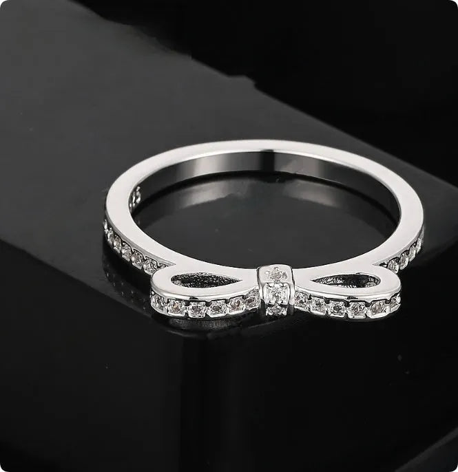 Close-up of a silver bow-shaped ring with sparkling clear zircon crystals on a person's finger.