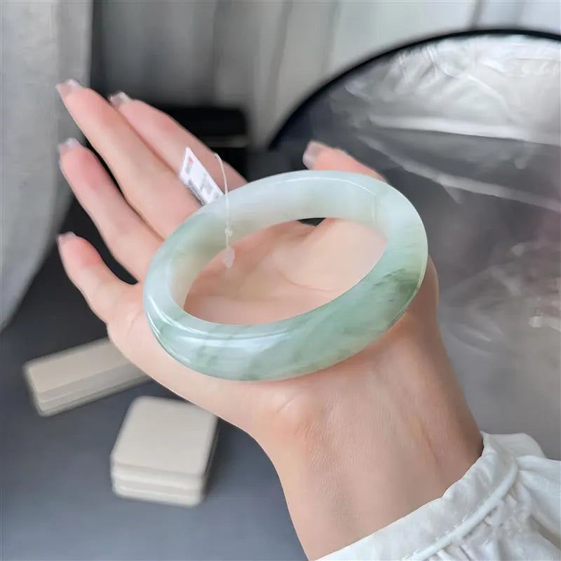 Clear ice-like jade bracelet with floating floral design and zodiac motif on a wrist.