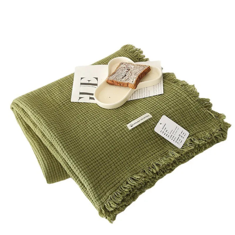 Four-layer gauze cotton blanket with tassel edging in avocado green, laid flat.