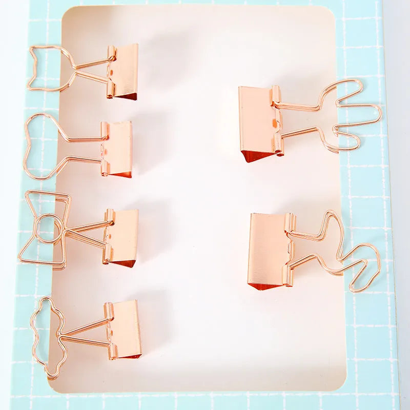 Small gold-plated metal office clip with a long tail, shown in decorative flamingo, love, cat, cactus, and bow shapes.